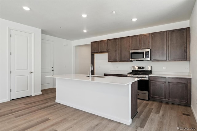 9662 Cathay St, Commerce City, CO 80022 - kitchen featuring light wood finished floors, an island with sink, stainless steel appliances, a sink, and dark brown cabinetry