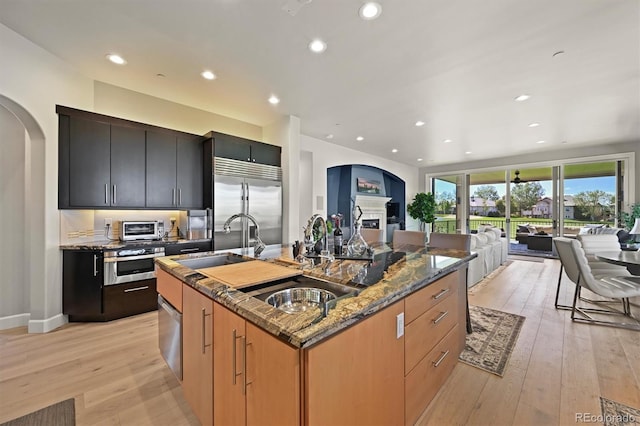 1287 Buffalo Ridge Rd, Castle Pines, CO 80108 - kitchen with stainless steel appliances, open floor plan, a sink, light wood-style flooring, and dark stone countertops