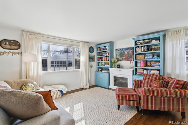 sitting room featuring wood finished floors, a fireplace with raised hearth, and baseboards