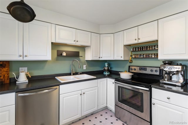 kitchen with light floors, a sink, appliances with stainless steel finishes, white cabinetry, and dark countertops