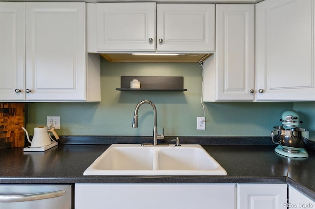 kitchen with dark countertops, white cabinets, dishwasher, and a sink