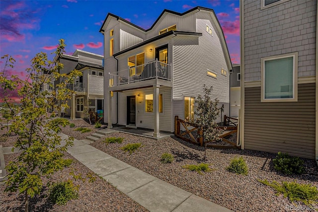 back of house at dusk featuring a patio area and a balcony