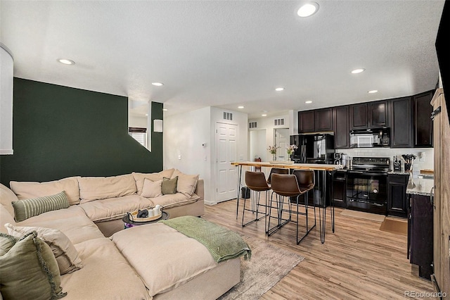 living room with light wood-type flooring, visible vents, and recessed lighting