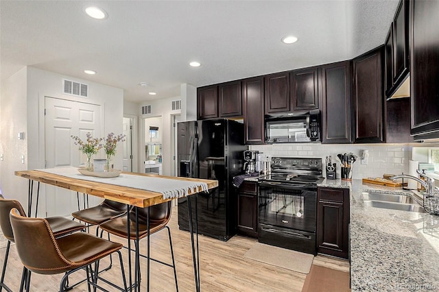 kitchen with light stone counters, visible vents, a sink, and black appliances