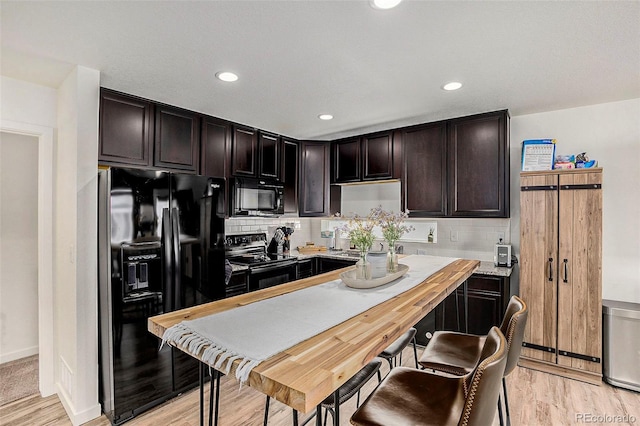 kitchen with decorative backsplash, light wood-style floors, black appliances, and dark brown cabinets