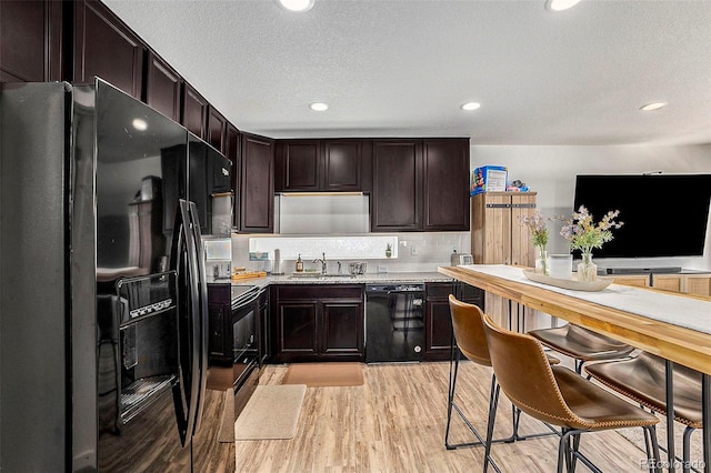 kitchen featuring light wood-type flooring, black appliances, light countertops, and a sink