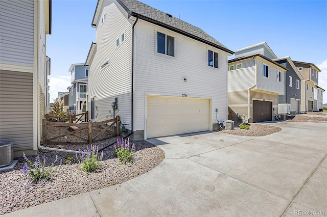 view of side of property featuring cooling unit, driveway, a residential view, and an attached garage