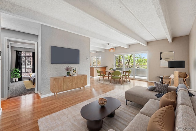living room with baseboards, beam ceiling, a textured ceiling, and light wood-style flooring