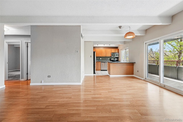 unfurnished living room featuring a textured ceiling, baseboards, beam ceiling, and light wood-style floors