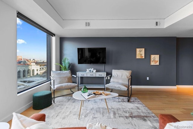 living room with wood finished floors, a raised ceiling, and baseboards