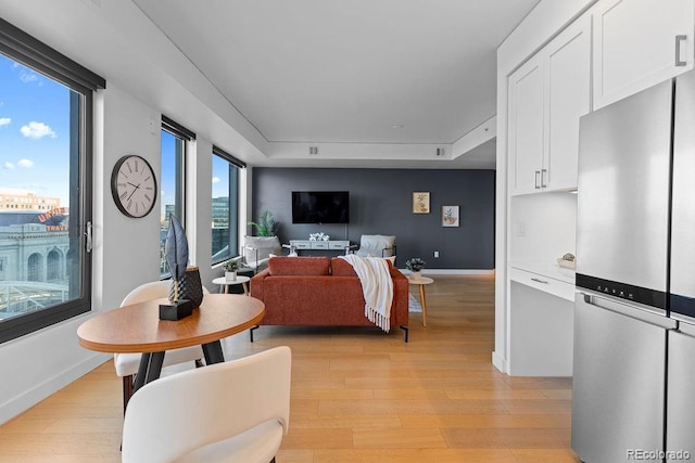 living area featuring light wood-style flooring, a tray ceiling, and baseboards