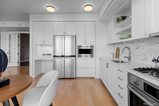 kitchen featuring appliances with stainless steel finishes, a sink, light countertops, white cabinetry, and tasteful backsplash