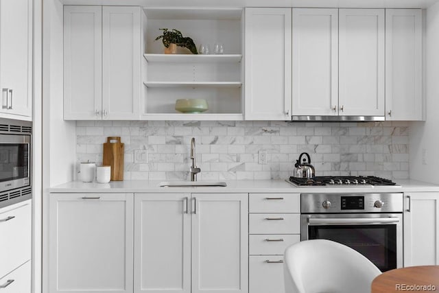 kitchen featuring appliances with stainless steel finishes, a sink, open shelves, and white cabinetry