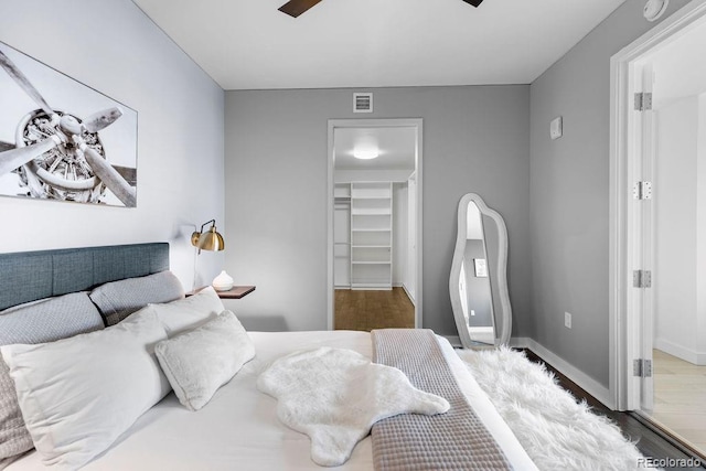 bedroom with a spacious closet, wood finished floors, a closet, and baseboards