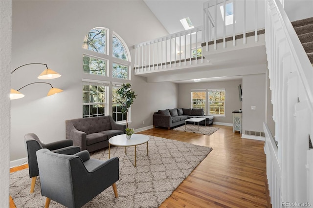 living area featuring visible vents, wood finished floors, a skylight, baseboards, and a towering ceiling