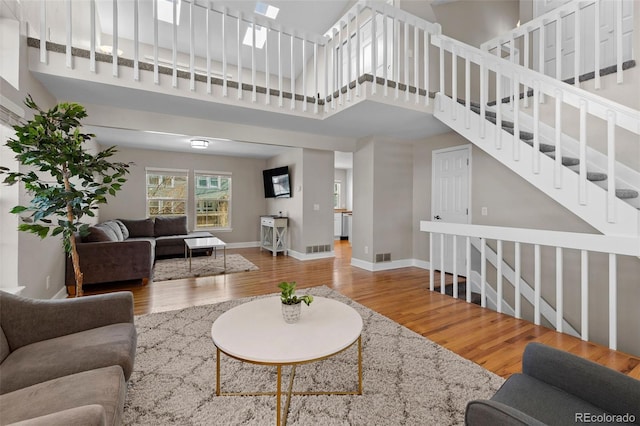 living area with a skylight, wood finished floors, baseboards, and a towering ceiling