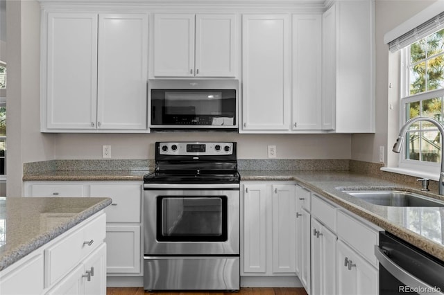 kitchen with white cabinetry, light stone countertops, appliances with stainless steel finishes, and a sink