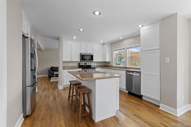 kitchen with light wood-type flooring, appliances with stainless steel finishes, white cabinets, and a center island