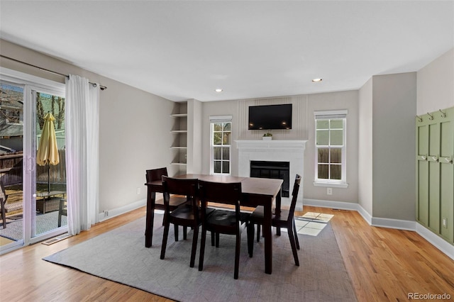 dining room with light wood finished floors, a glass covered fireplace, recessed lighting, and baseboards