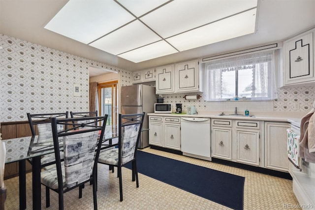 kitchen with a sink, white appliances, light countertops, and wallpapered walls