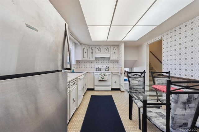 kitchen with white appliances, premium range hood, wallpapered walls, a sink, and light countertops