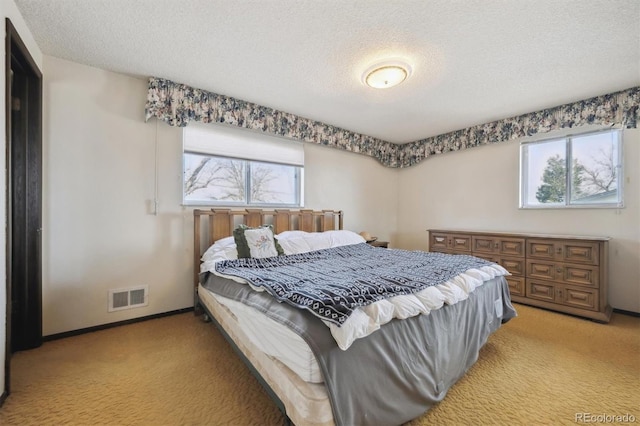 bedroom featuring baseboards, light colored carpet, visible vents, and a textured ceiling