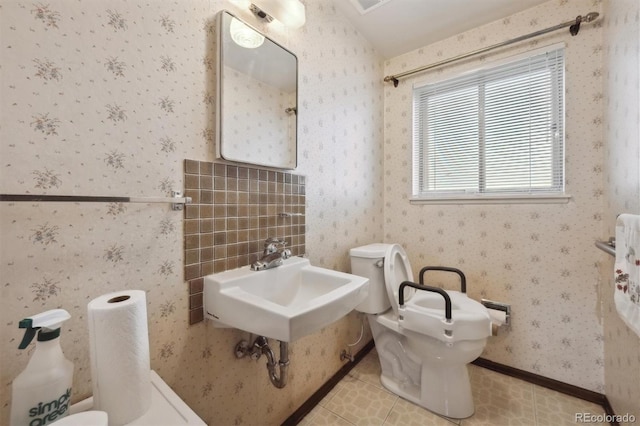 half bath with tile patterned floors, toilet, a sink, wallpapered walls, and baseboards