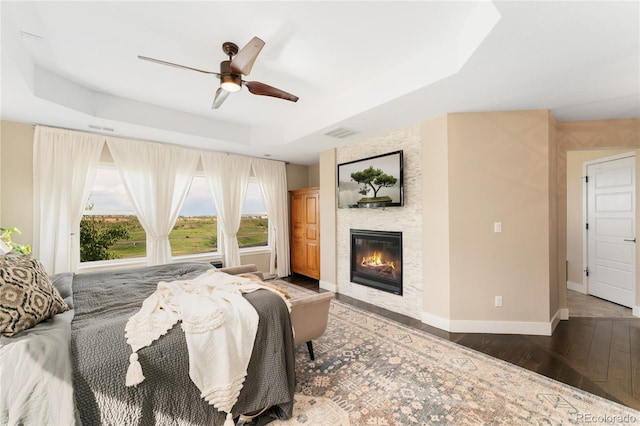 19429 W 88th Dr, Arvada, CO 80007 - bedroom featuring a raised ceiling, wood-type flooring, a stone fireplace, and a ceiling fan