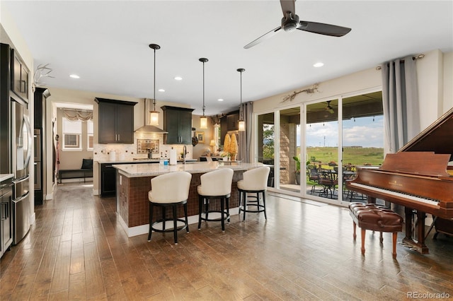 19429 W 88th Dr, Arvada, CO 80007 - kitchen featuring wall chimney range hood, an island with sink, stainless steel refrigerator with ice dispenser, dark wood finished floors, and a kitchen bar