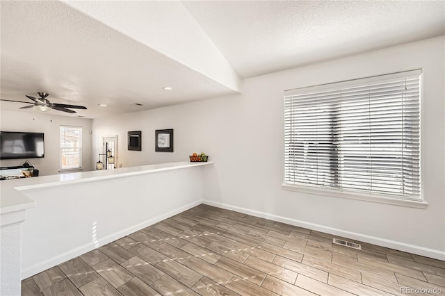 kitchen with ceiling fan, lofted ceiling, kitchen peninsula, and a textured ceiling