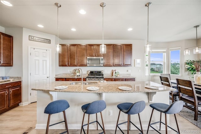 3620 Sandoval St, Brighton, CO 80601 - kitchen with appliances with stainless steel finishes, light wood finished floors, a kitchen breakfast bar, hanging light fixtures, and light stone counters