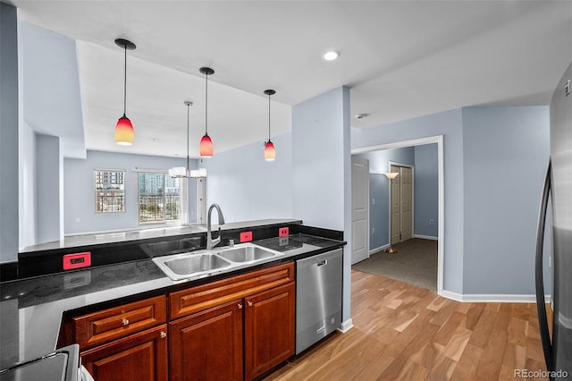 kitchen with hanging light fixtures, light wood-style flooring, a sink, dark countertops, and appliances with stainless steel finishes