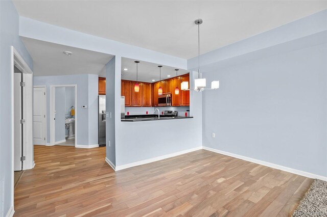 kitchen featuring light wood-style flooring, baseboards, hanging light fixtures, dark countertops, and appliances with stainless steel finishes