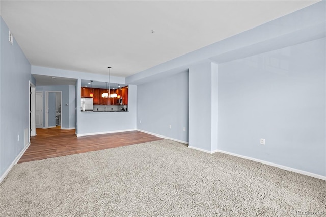 unfurnished living room with an inviting chandelier, baseboards, and dark carpet