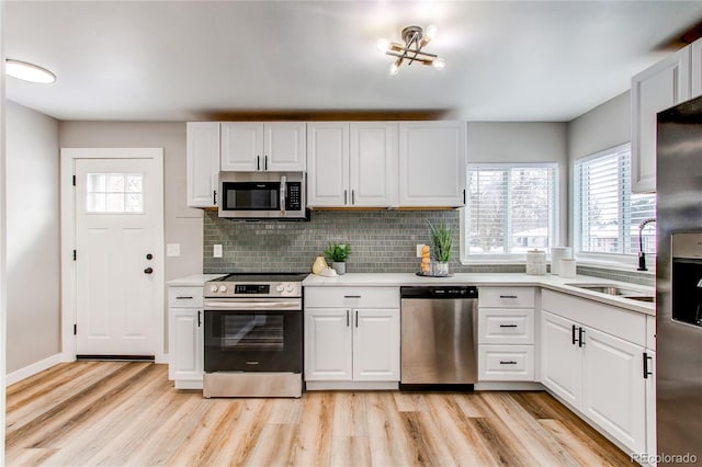 kitchen featuring appliances with stainless steel finishes, sink, white cabinets, and light wood-type flooring