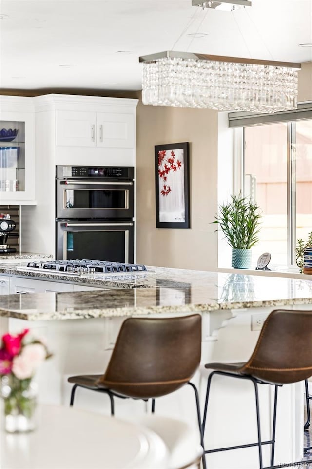 kitchen with stainless steel double oven, light stone counters, a kitchen breakfast bar, and white cabinets