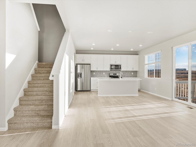 kitchen with appliances with stainless steel finishes, white cabinetry, an island with sink, decorative backsplash, and light wood-type flooring