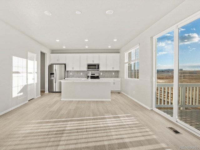 kitchen with white cabinets, appliances with stainless steel finishes, a center island with sink, and tasteful backsplash