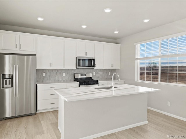 kitchen featuring a center island with sink, appliances with stainless steel finishes, white cabinets, light hardwood / wood-style flooring, and sink