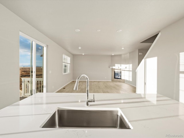 kitchen featuring light stone countertops, sink, light hardwood / wood-style flooring, and a fireplace