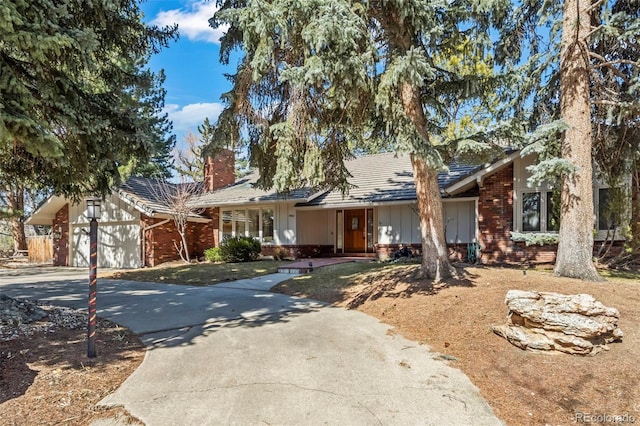 view of front of home with brick siding, an attached garage, concrete driveway, and a chimney