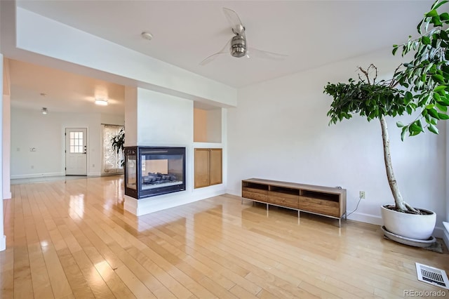 living room featuring ceiling fan, a multi sided fireplace, and light hardwood / wood-style floors