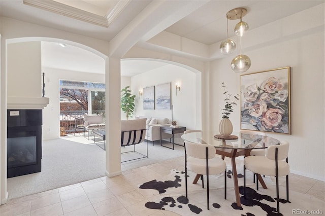 dining room featuring arched walkways, ornamental molding, a raised ceiling, light colored carpet, and light tile patterned floors