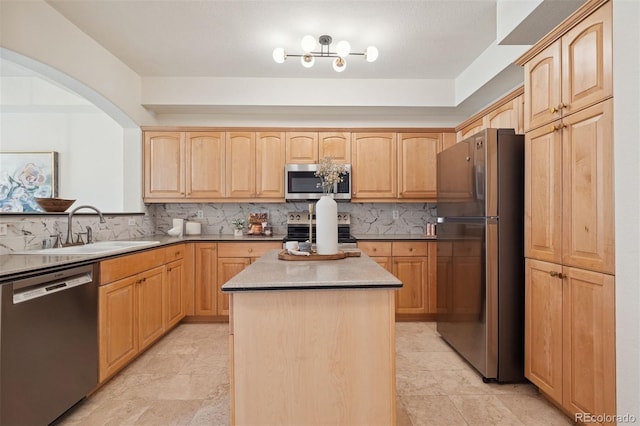kitchen featuring stainless steel appliances, a sink, light brown cabinets, tasteful backsplash, and a center island