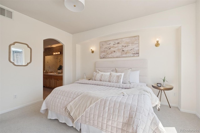 bedroom featuring carpet, arched walkways, baseboards, and ensuite bath