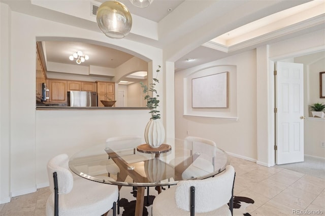dining space with arched walkways, baseboards, and a raised ceiling