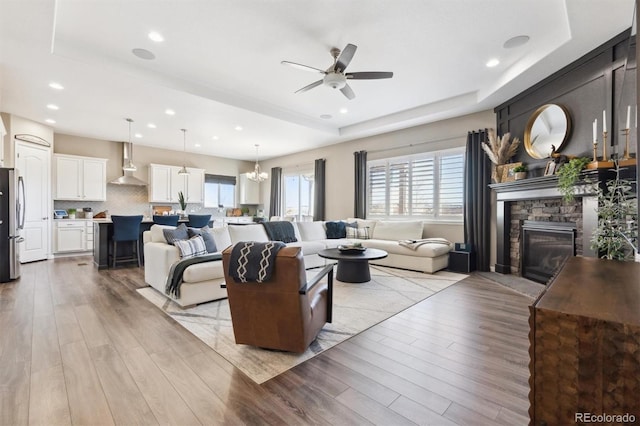 living room with a tray ceiling, plenty of natural light, a stone fireplace, and wood finished floors