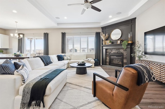 living area featuring a raised ceiling, a fireplace, wood finished floors, and recessed lighting