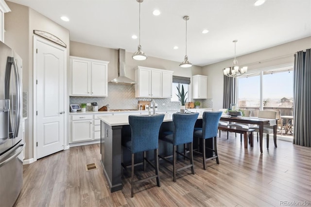 kitchen featuring stainless steel appliances, wood finished floors, light countertops, wall chimney exhaust hood, and a center island with sink