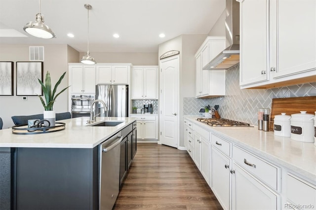 kitchen featuring visible vents, stainless steel appliances, wall chimney range hood, white cabinetry, and a sink